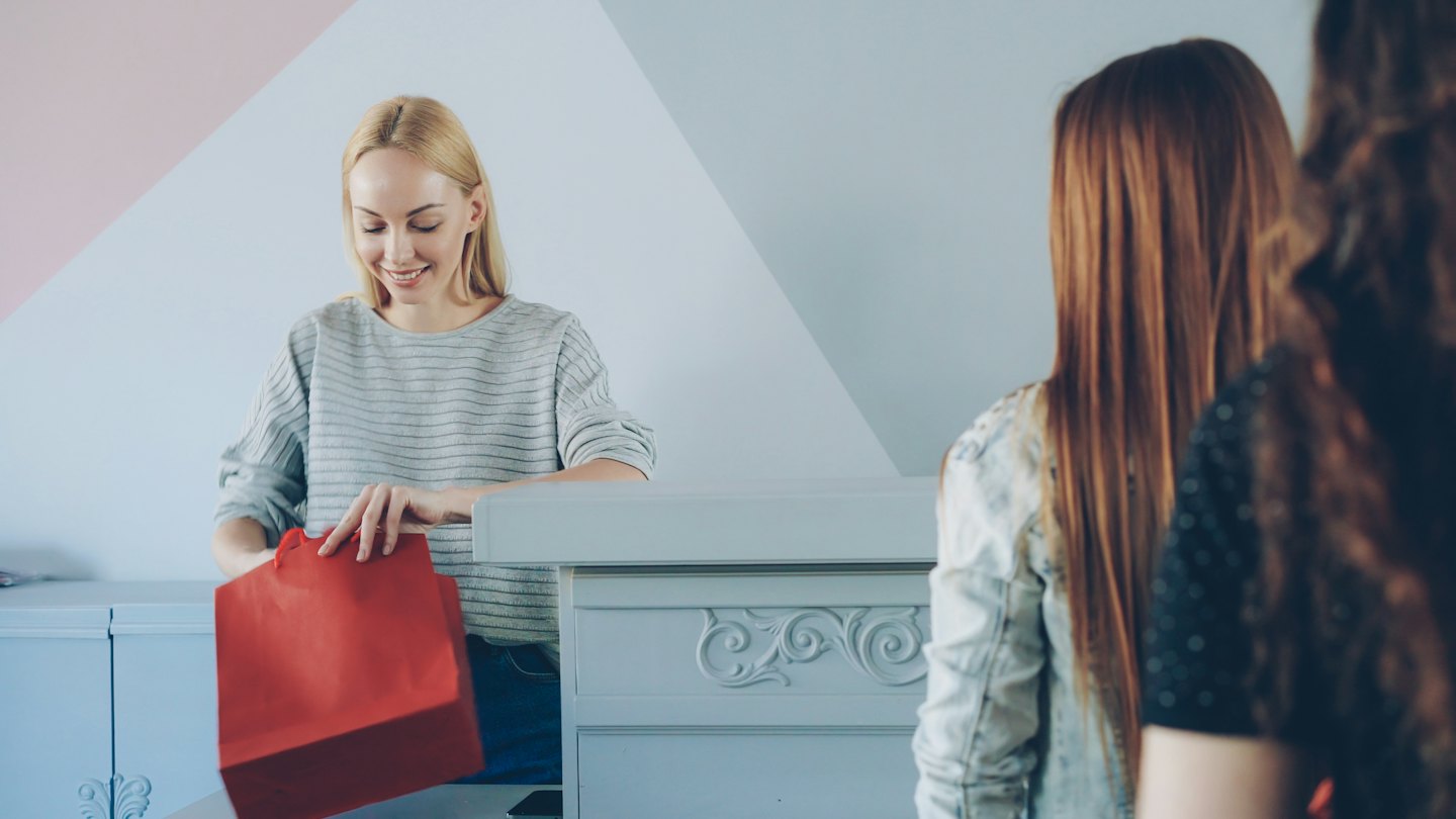 Salesperson smiling while placing item into a red shopping bag.